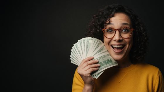 Close crop of creator holding a fan of cash with a shocked expression